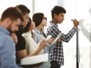 Male high school pupil writing on whiteboard in class