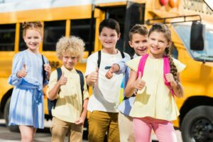 group of happy pupils looking at camera and showing thumbs up in front of school bus