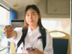 Young Asian woman showing credit card while sitting inside public bus transport