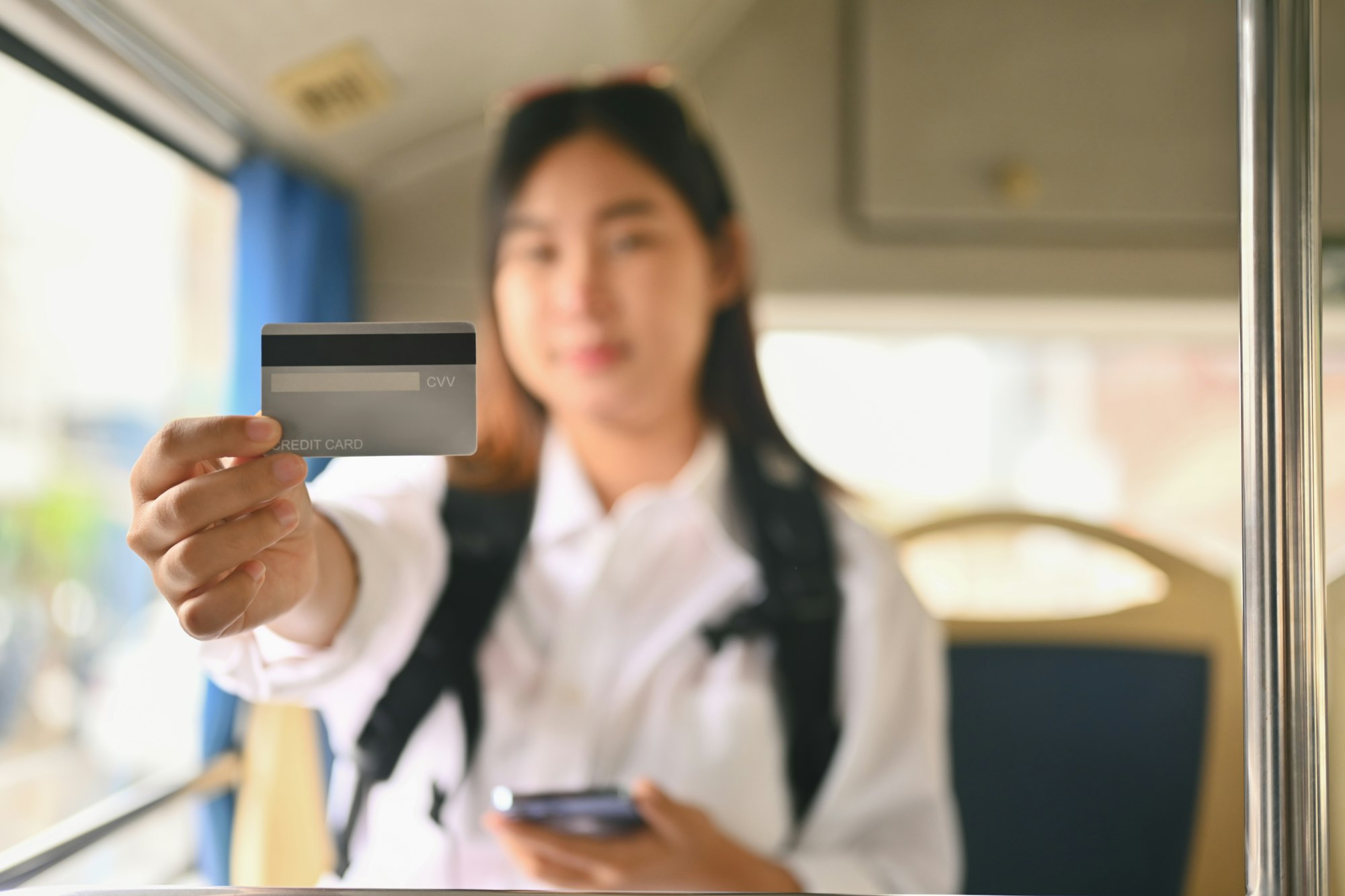 Young Asian woman showing credit card while sitting inside public bus transport
